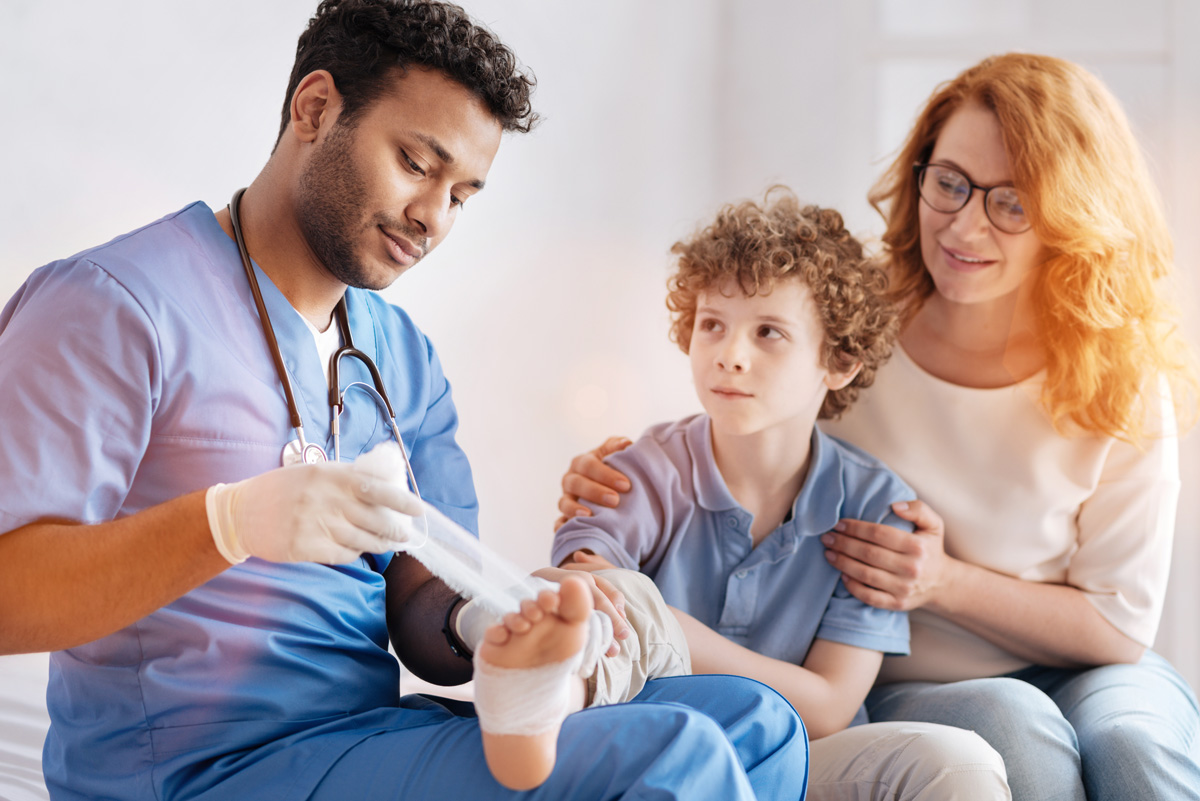 A doctor wrapping a child’s foot in gauze with his mother sitting next to him in El Paso.